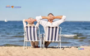 2 personen in een strandstoel op het strand die met hun handen in de nek naar de zee kijken